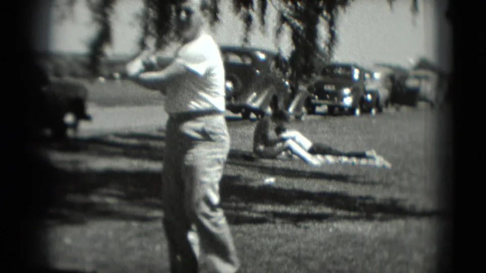 A side view shows the golfer mid-swing on a sunlit grassy course in Washington, DC, with 1970s cars and a reclining figure in the background.