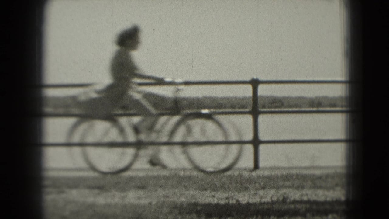 The cyclist passes through the frame along the waterfront, partly soft from motion and 8mm focus, with railing and water visible.