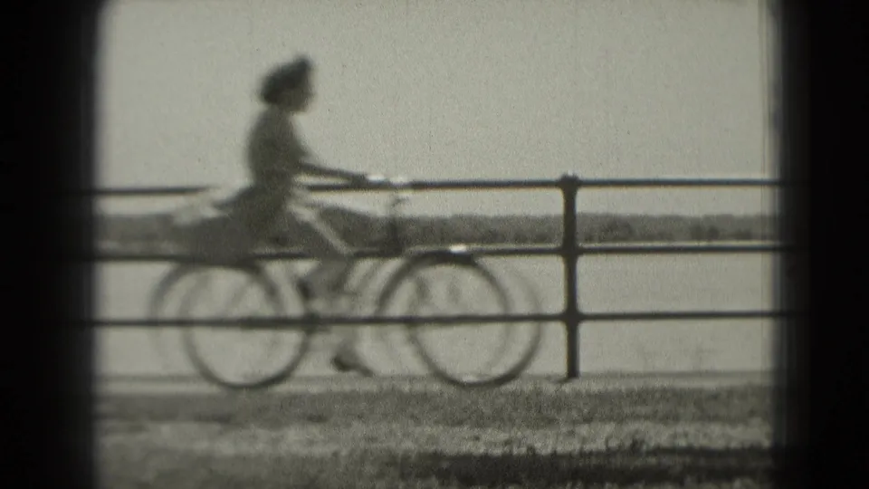 The cyclist passes through the frame along the waterfront, partly soft from motion and 8mm focus, with railing and water visible.