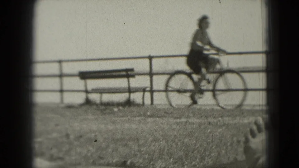 The cyclist moves past a waterfront bench in Washington DC, framed by railing, water, soft focus, and visible 8mm film edges.