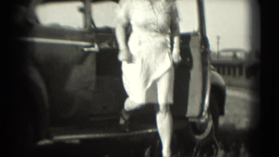 The woman in a light dress steps down from the sedan, with the open passenger door behind her.