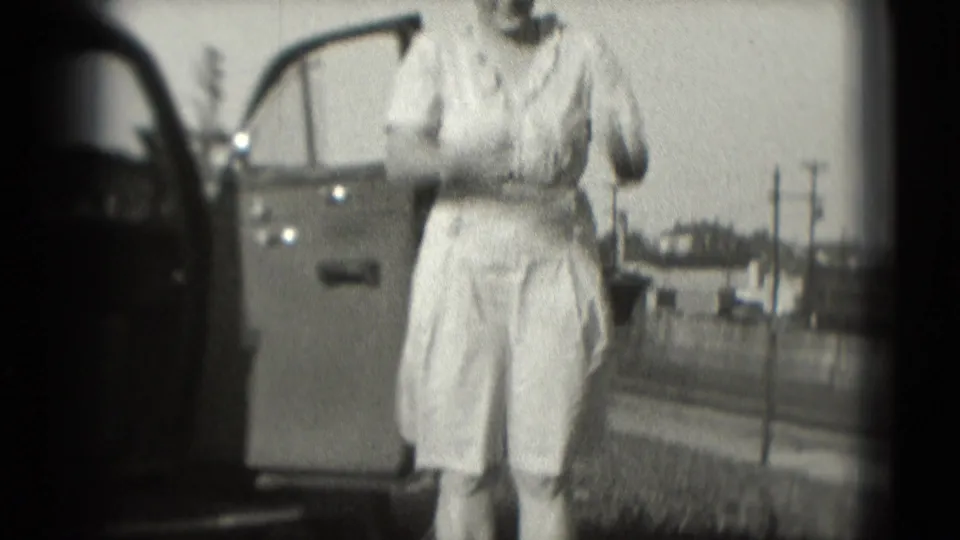 A smiling woman stands beside the open sedan door in a 1975 Washington, DC home-movie frame.