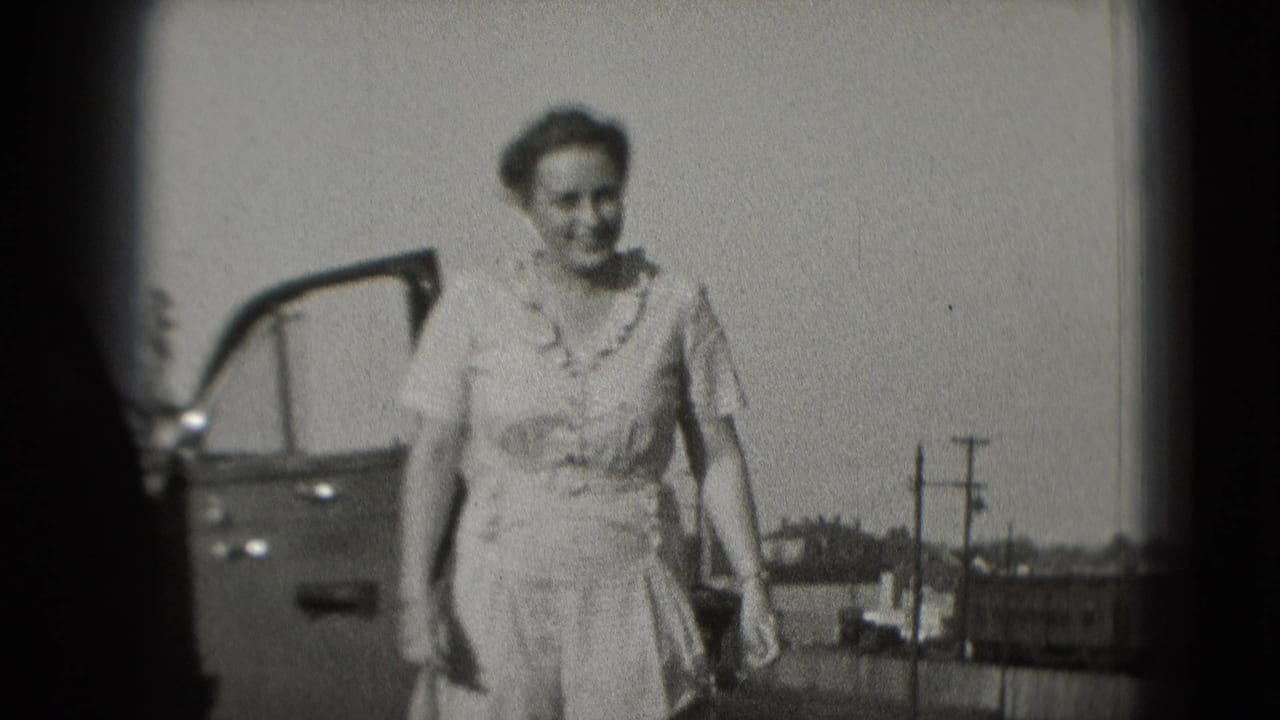 In 1975 Washington, DC home-movie footage, a woman in a light dress smiles while walking beside an open car door.