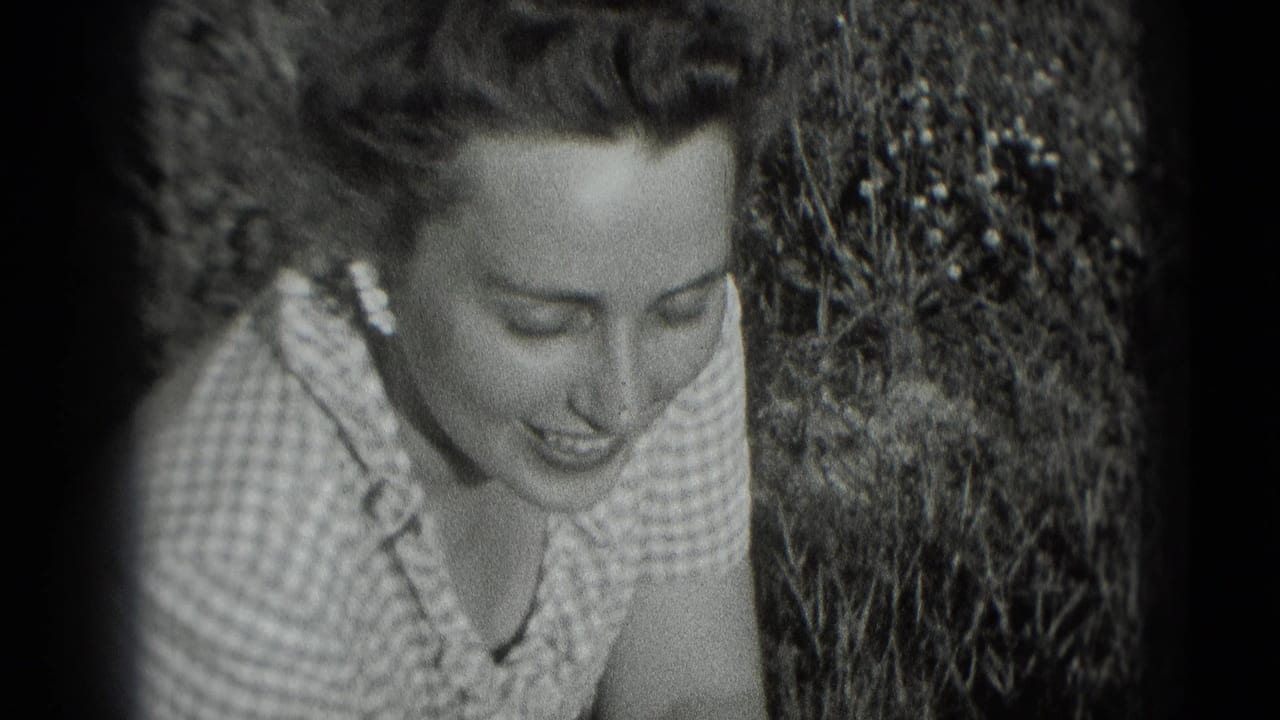 Woman in a checkered dress smiles while leaning among garden plants.