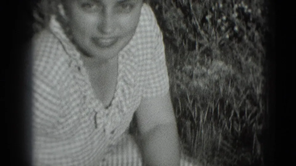 The woman looks up toward the camera from the garden, framed closely with plants at her side.