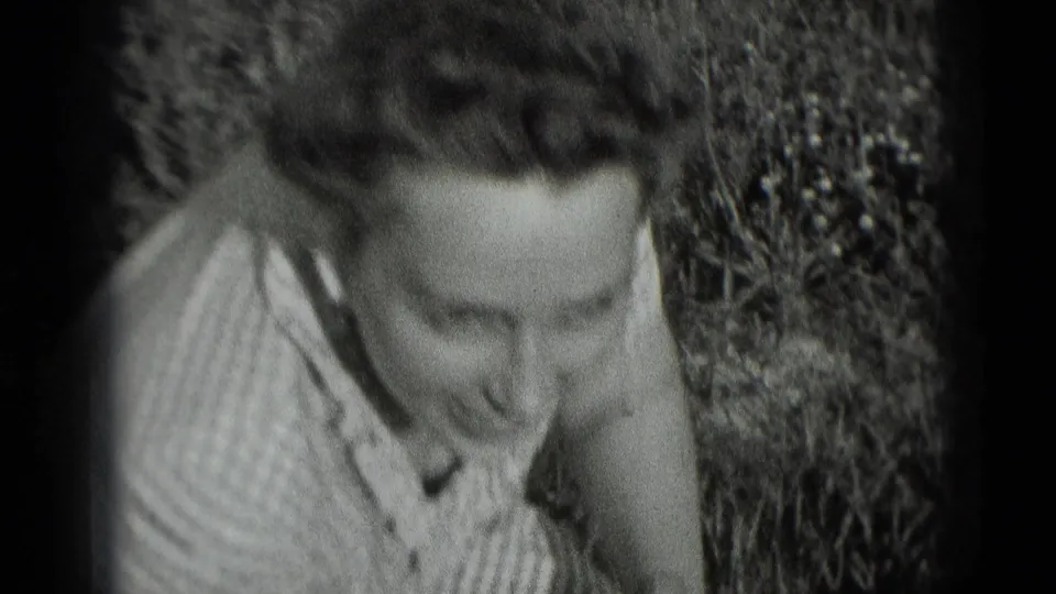 The woman smiles broadly while leaning forward in the garden, captured in soft 8mm home-movie texture.