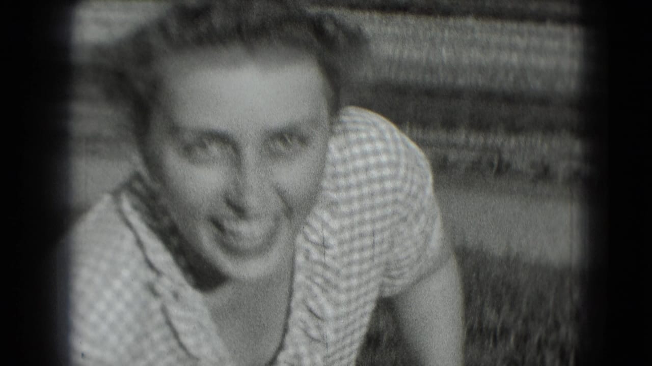 Young woman in a checkered dress leaning toward the camera outdoors.