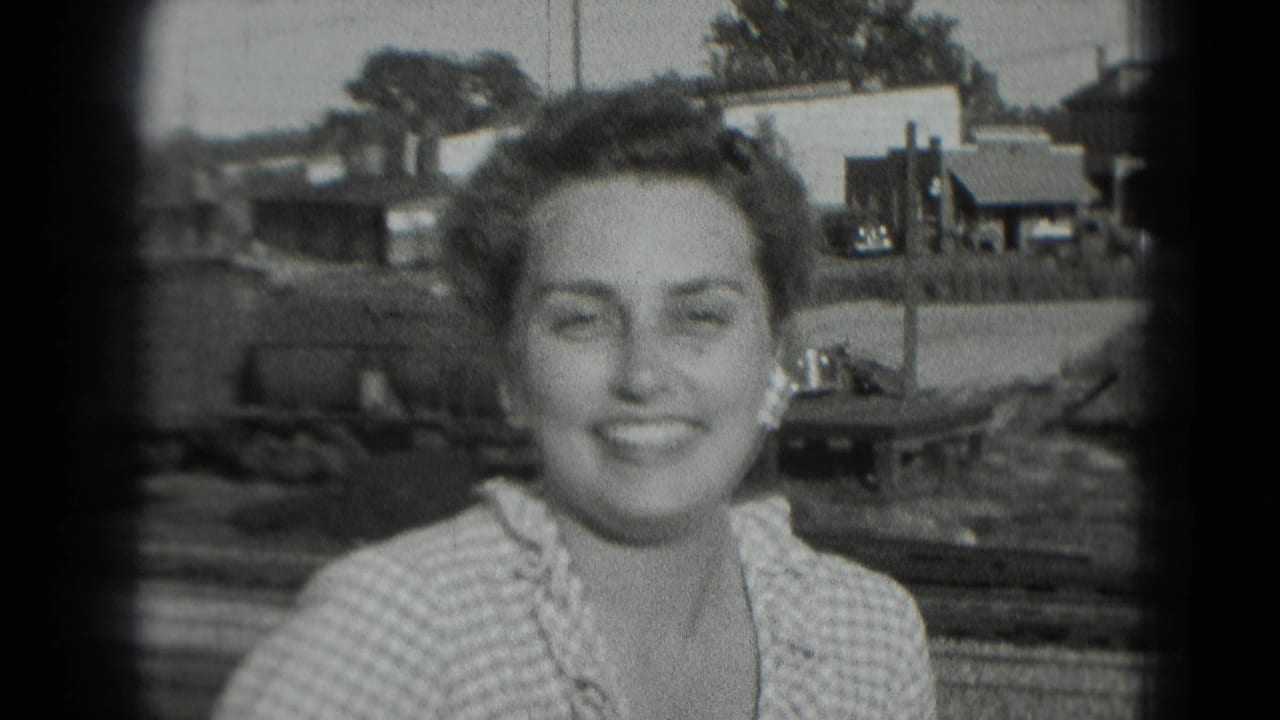 Young woman smiling outdoors with houses and trees behind her.