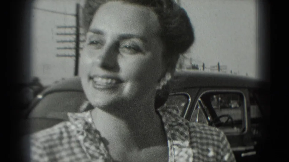 The woman smiles while turning slightly away from the camera, with the car and street details behind her.
