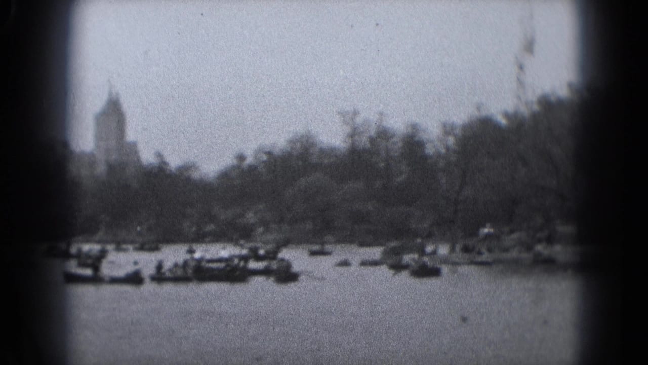 1975 Washington DC home-movie frame showing small boats on a lake, a wooded shore, and distant urban buildings.