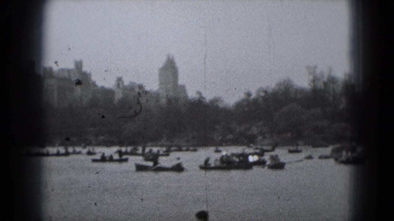 Soft 8mm frame of a Washington DC lakeside view, with rowboats on the water and a distant tower-like building above trees.