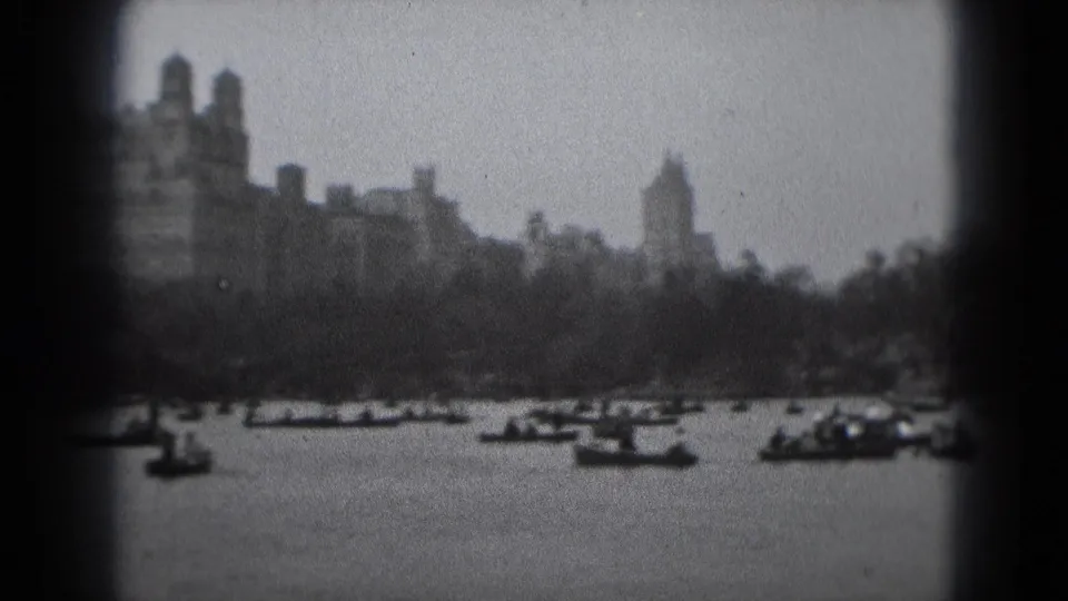 1975 Washington DC visitor footage frame showing rowboats in front of trees and large distant buildings across the water.