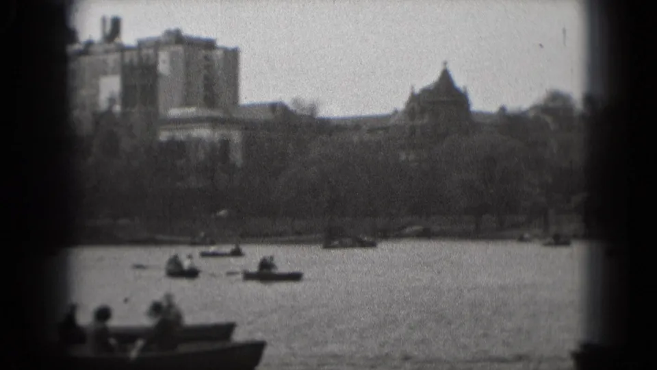 Washington, DC park view from 1975 with small boats on the water and a castle-like building beyond the trees.