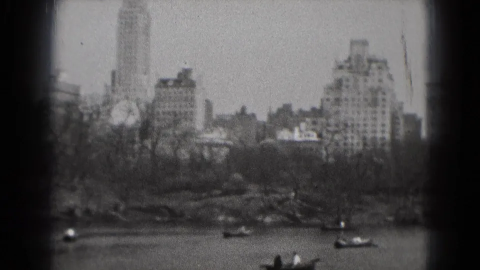 1975 8mm view of a Washington, DC park lake with boats in the foreground and city buildings behind the trees.