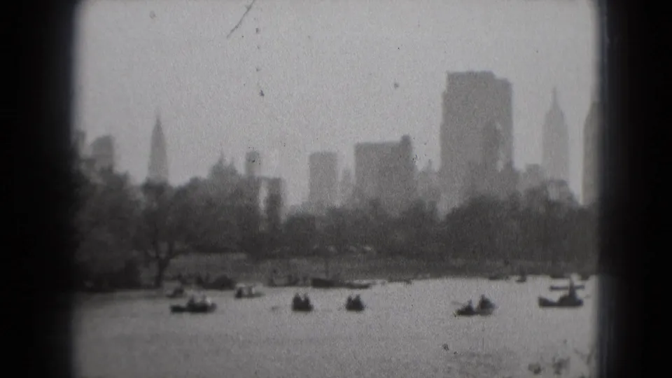 Washington DC waterfront scene from 1975 8mm film, showing scattered boats, trees, and distant buildings under cloudy haze.