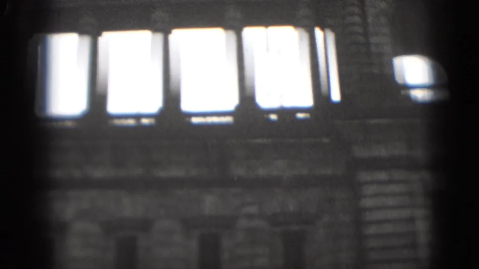 1975 Washington, DC home-movie frame with tall glowing windows above a dark, textured stone exterior.