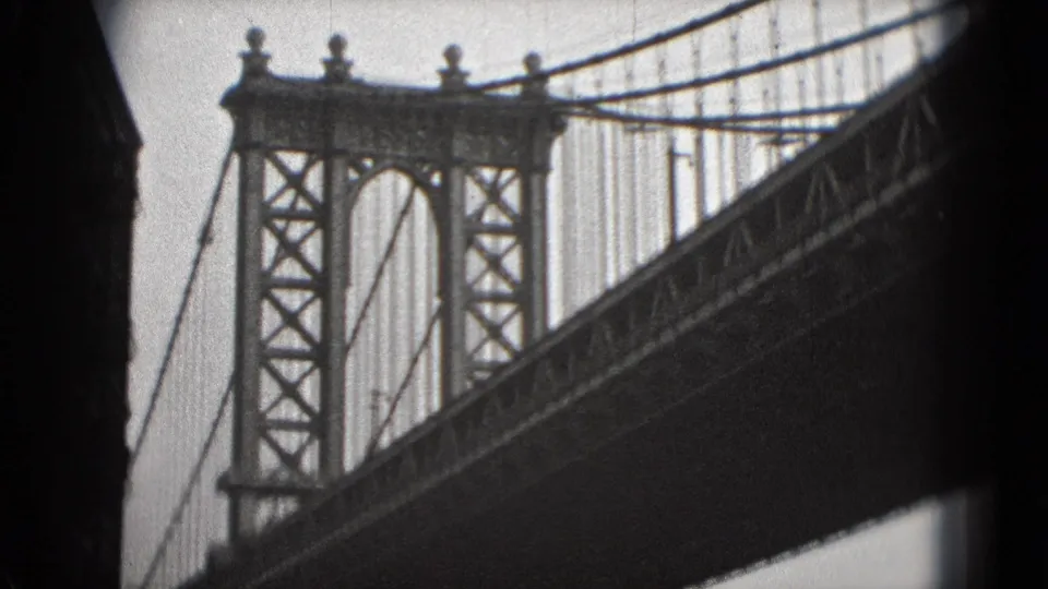 Black-and-white 8mm view of a suspension bridge tower and cable lines, with the bridge deck cutting diagonally across the frame.