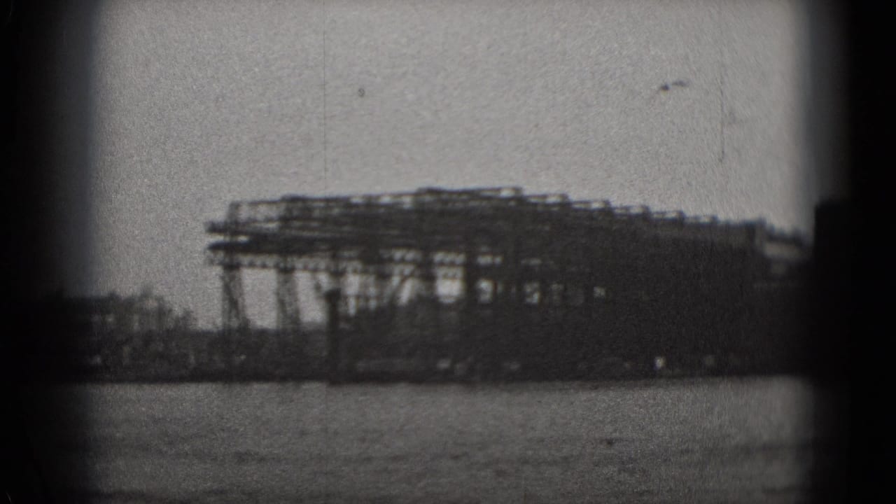 Black-and-white 1975 Washington DC 8mm view of a low industrial waterfront structure across the water under a hazy sky.