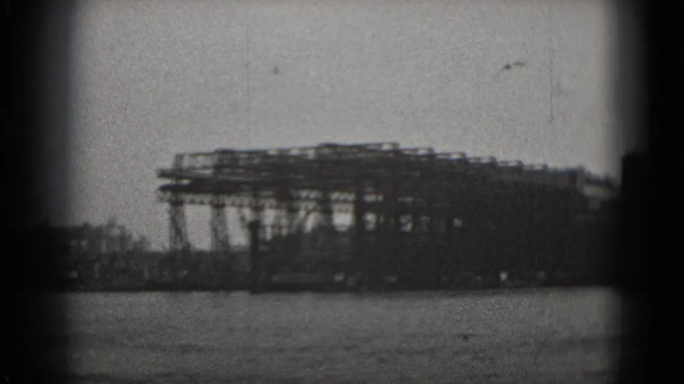 Black-and-white 1975 Washington DC 8mm view of a low industrial waterfront structure across the water under a hazy sky.