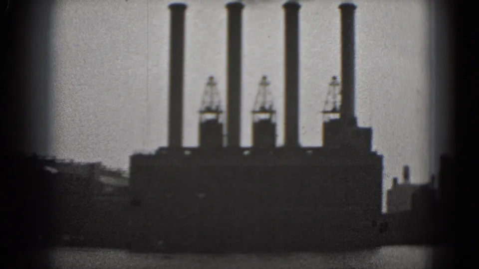 Black-and-white 1975 Washington DC 8mm frame of an industrial building with four tall smokestacks and cranes near the waterfront.