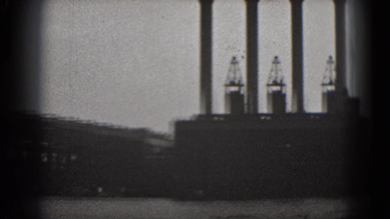 Distant industrial waterfront with smokestacks seen through dark vertical framing.