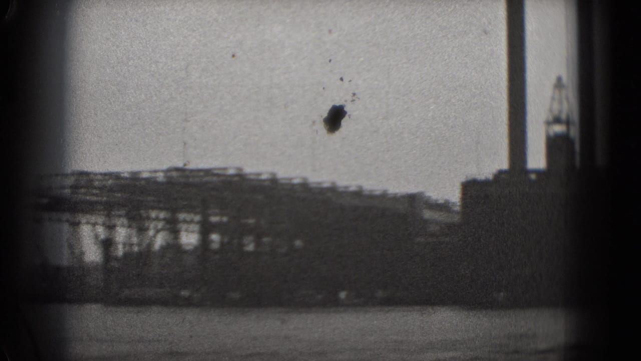 Low industrial buildings and crane-like structures across a body of water.