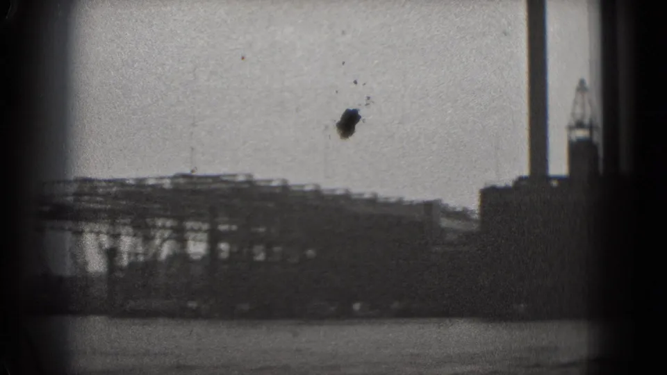 Black-and-white 8mm frame from Washington DC showing low waterfront industrial structures and crane-like forms beyond the water.