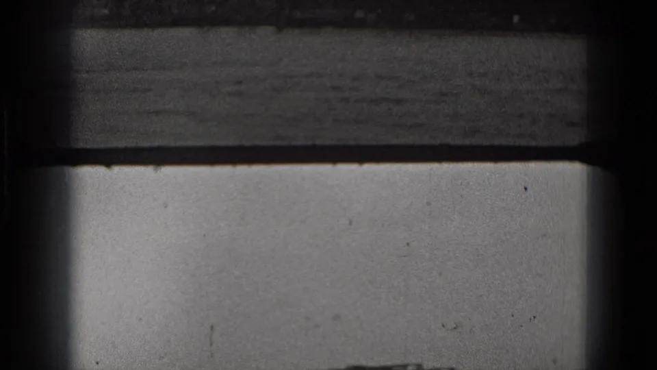Grainy 1975 Washington DC 8mm frame showing a low industrial waterfront across water, bordered by dark foreground edges.