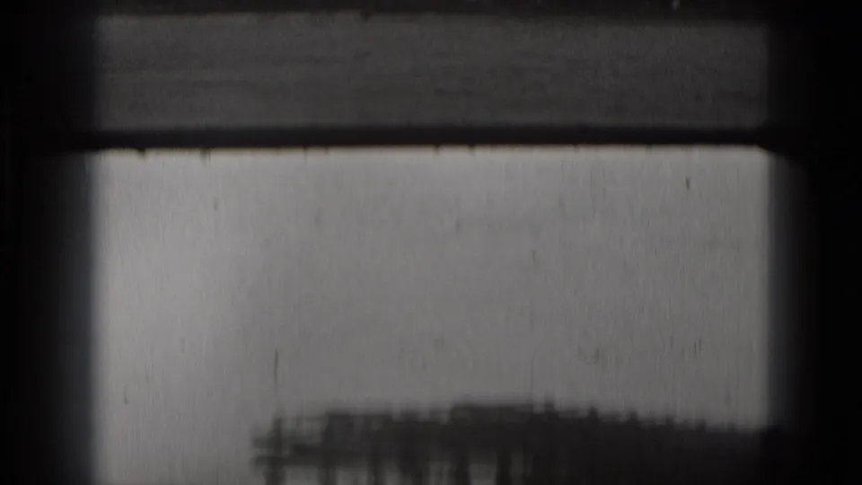 Soft black-and-white 8mm opening frame, partially obscured by film borders, with a faint waterfront structure near the lower edge.