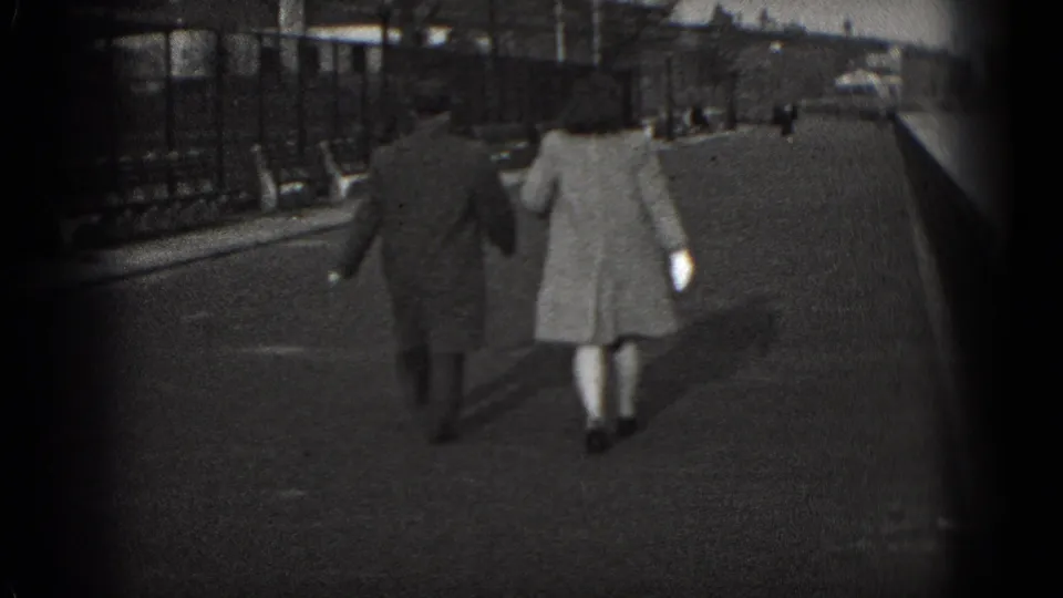 A man and woman, seen from behind, walk along a Washington, DC waterfront path in 1975 home-movie footage.