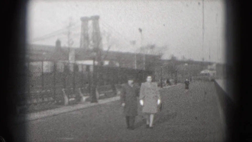 Overexposed 1975 8mm frame of the couple continuing along the Washington, DC waterfront promenade near a suspension bridge.