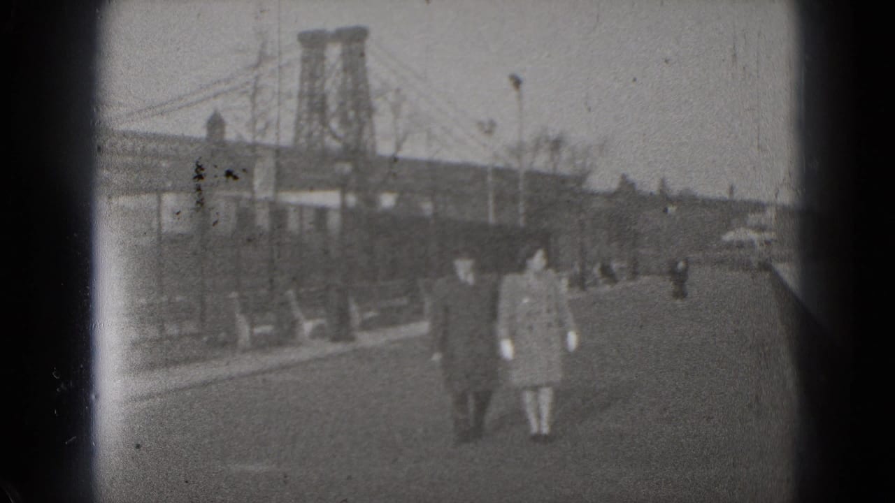 1975 Washington, DC home-movie frame showing pedestrians on a city street with bridge towers and roadway traffic in the background.