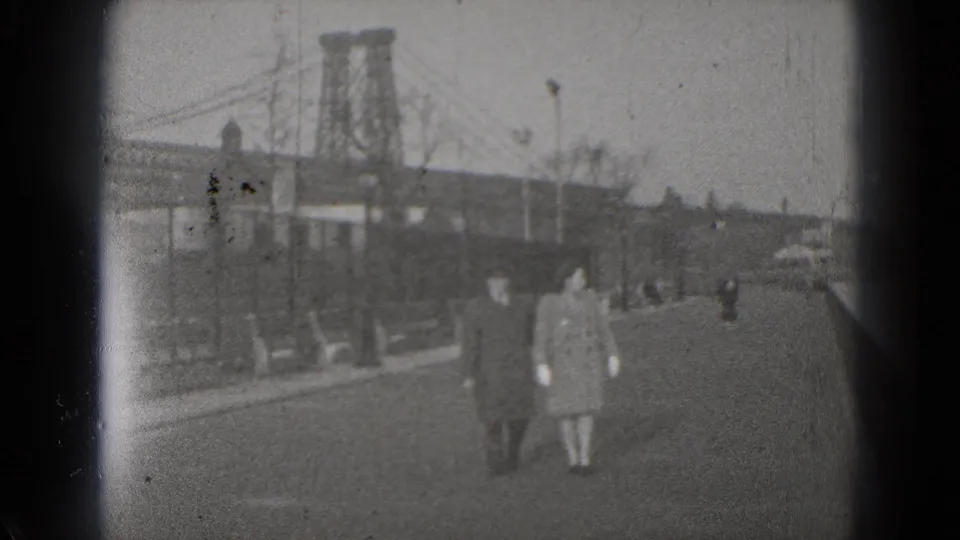 1975 Washington, DC home-movie frame showing pedestrians on a city street with bridge towers and roadway traffic in the background.