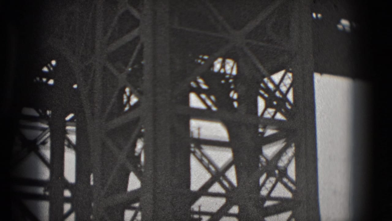 Black-and-white 8mm frame with close steel bridge trusses and vertical supports, likely from the Washington, DC bridge scene.