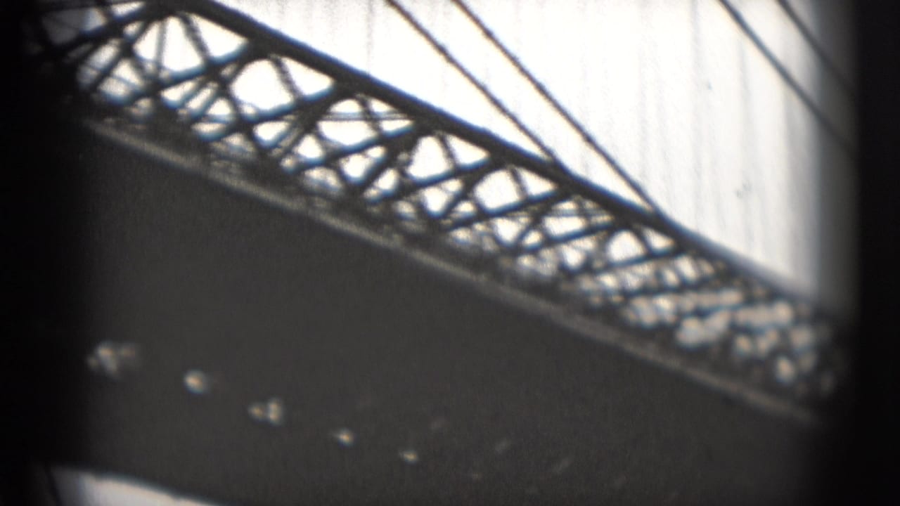 1975 8mm Washington DC waterfront view looking up at a bridge truss, cables, and dark underside against a bright sky.