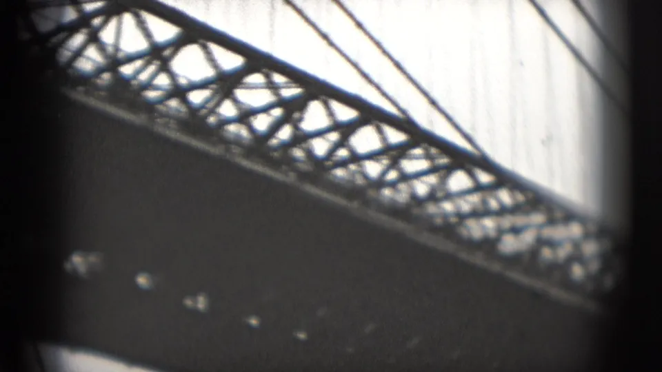 1975 8mm Washington DC waterfront view looking up at a bridge truss, cables, and dark underside against a bright sky.