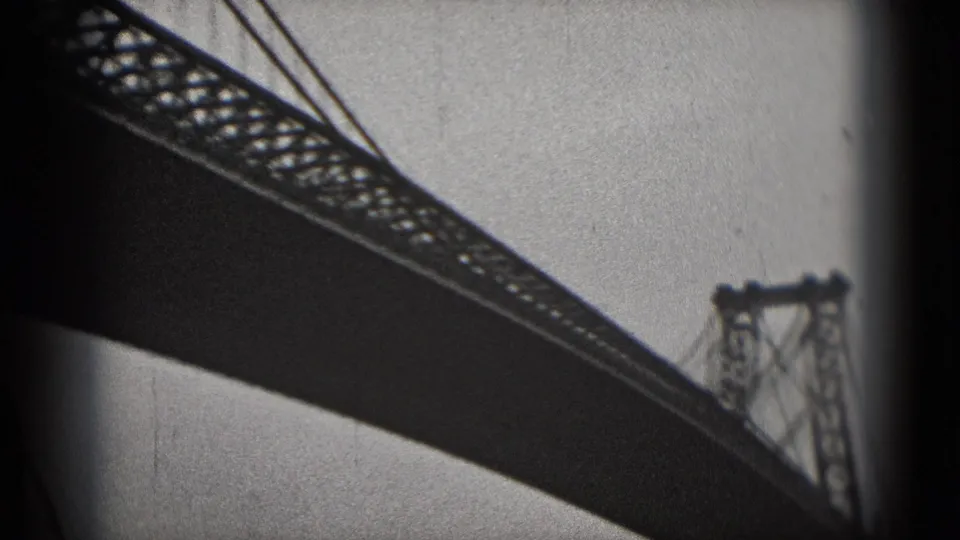 1975 8mm Washington DC waterfront shot with a diagonal bridge span, cables, distant tower, and riverfront background.