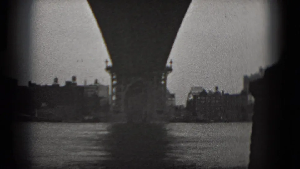 1975 8mm Washington DC waterfront view beneath the bridge, showing a central pier, river water, and distant shoreline buildings.