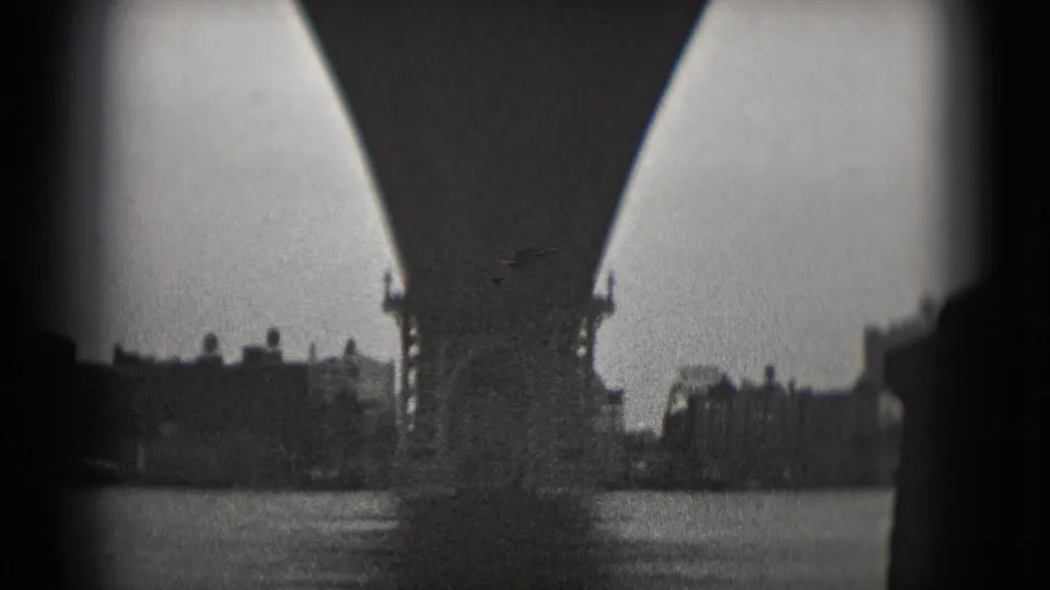 1975 Washington, DC 8mm frame showing bridge arches or supports with water and distant buildings beyond.