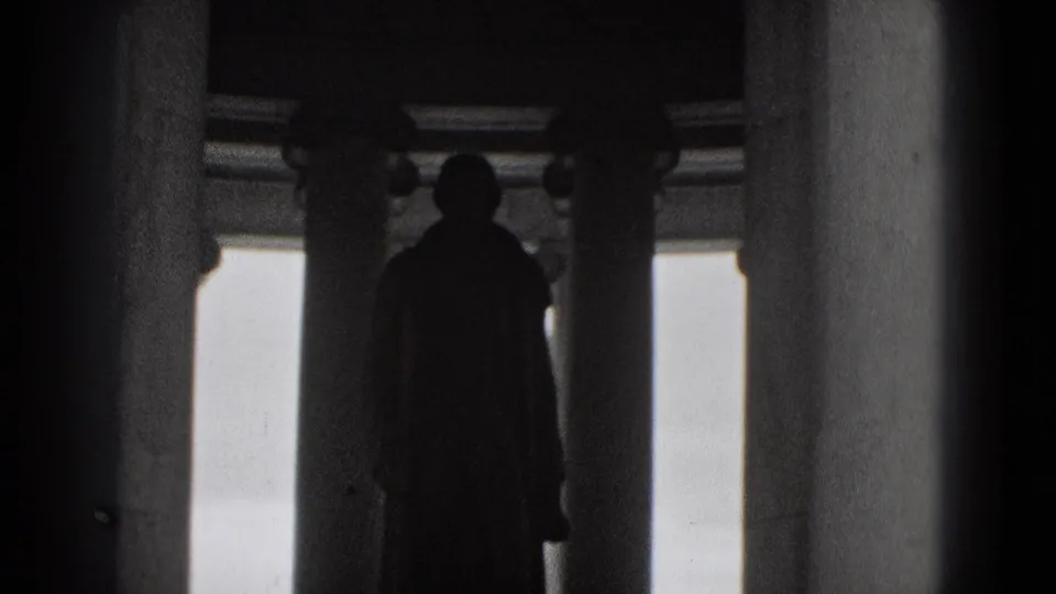 A black-and-white 8mm frame shows a woman in silhouette standing among columns inside a Washington, DC monument.