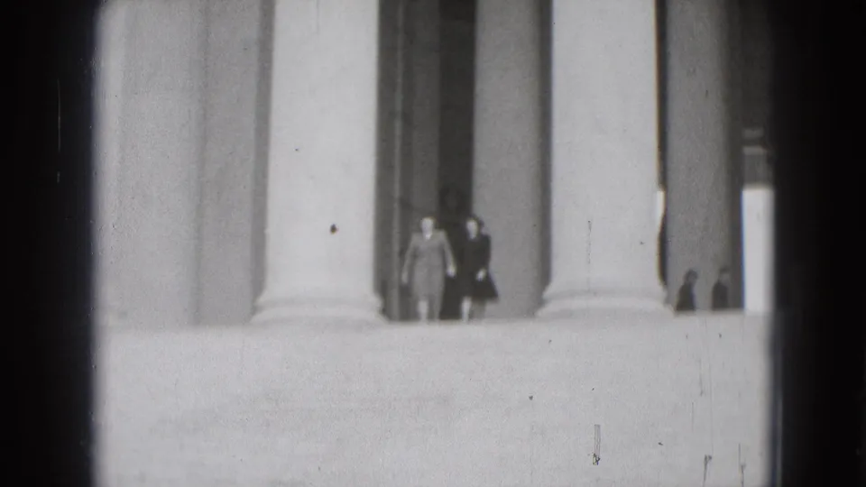Two distant women appear to walk through a large columned Washington DC landmark space in 1975 home-movie footage.
