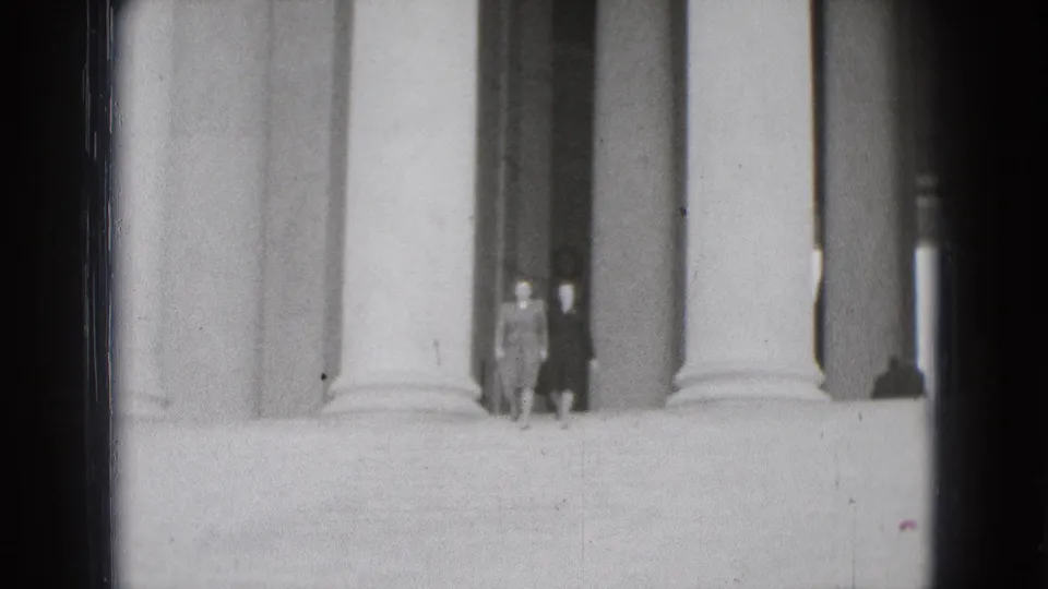 Two women in 1970s attire walk between tall columns at a Washington DC historical building in home-movie footage.