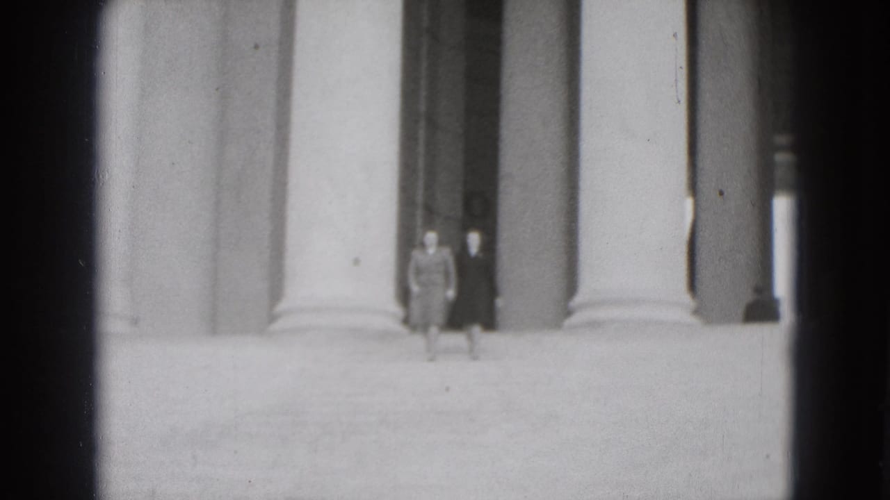 Two women stand or walk on broad steps beneath tall columns.