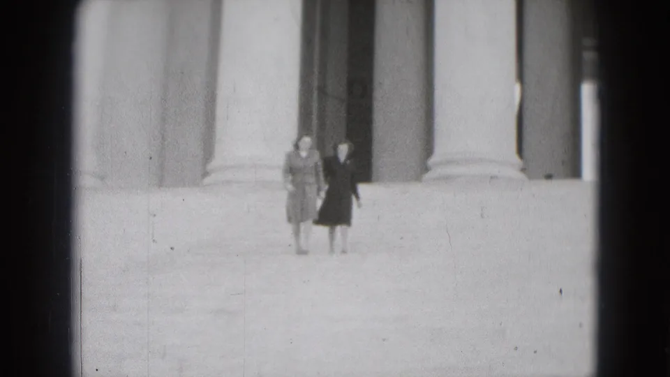 Two women walk toward the camera on monumental steps in Washington DC, with large columns behind them and visible 8mm film wear.