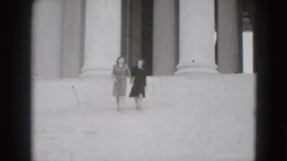 In 1975 Washington DC home-movie footage, two adult women appear small in frame near classical columns and wide stone steps.
