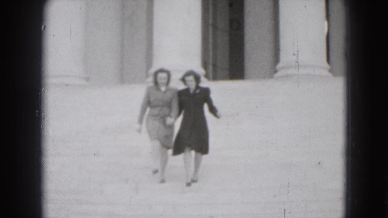Two women walk hand-in-hand down stone steps in front of tall columns.