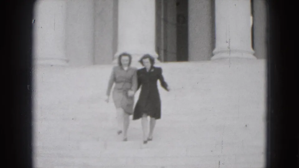Two adult women walk hand-in-hand toward the camera on broad Washington DC steps, with classical columns behind them.