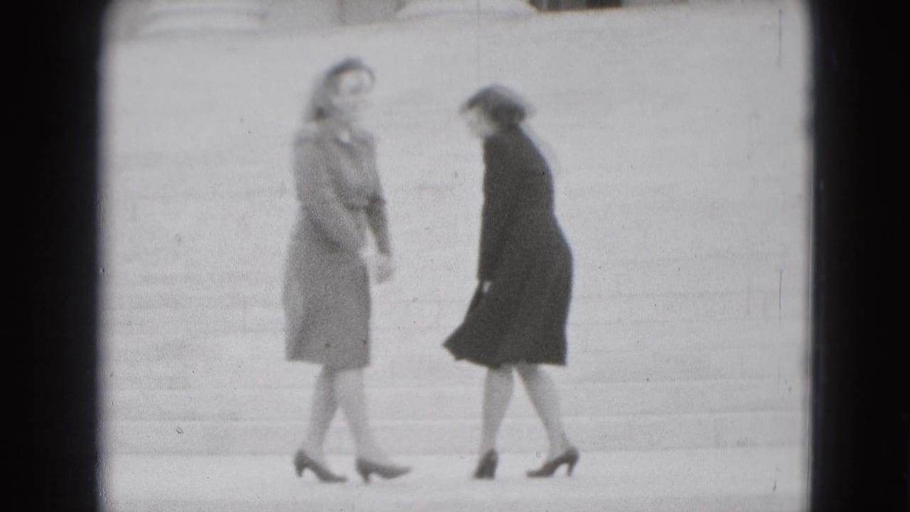 Two adult women in coats appear to turn toward each other on broad stone steps, with wind and motion softening the frame.