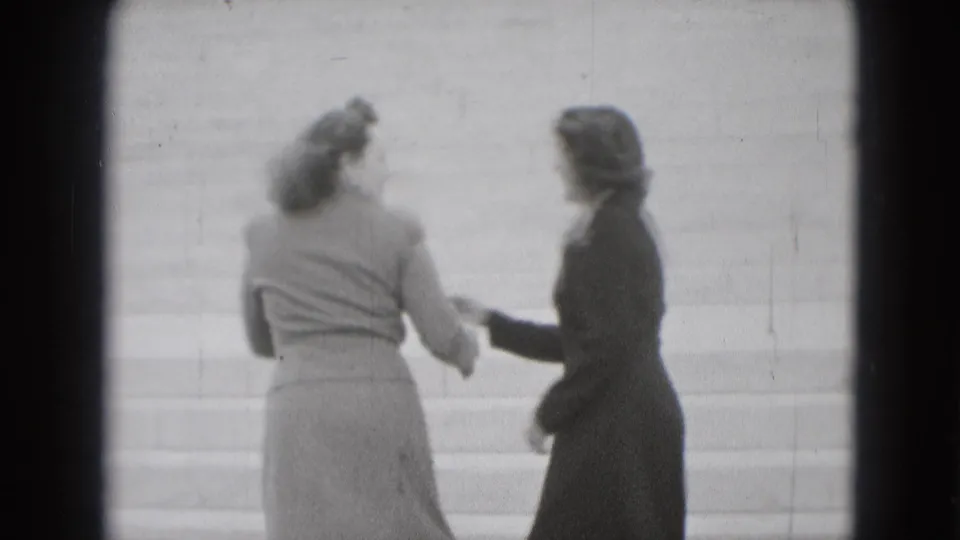 Two adult women pause or turn toward each other on broad Washington, DC steps, with one figure seen mostly from behind.