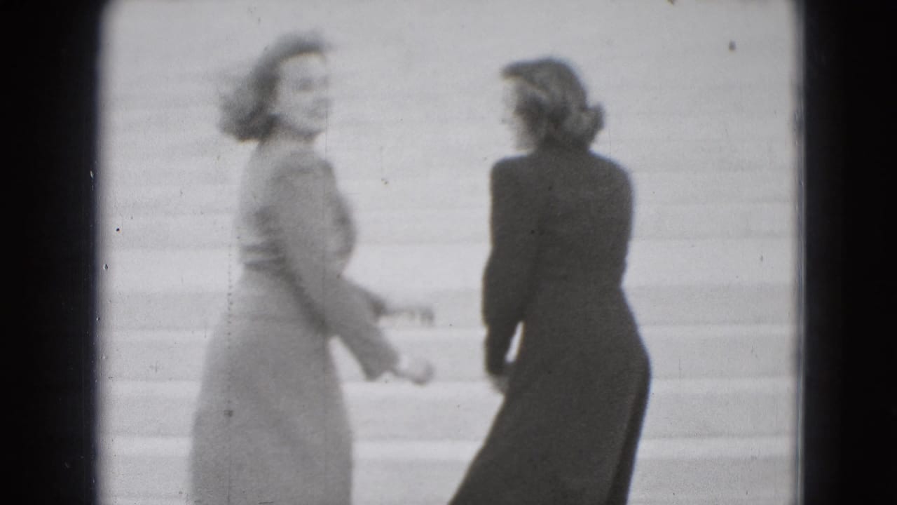 Two young women in 1975 Washington, DC home-movie footage stand playfully on broad stone steps, one looking back toward the camera.